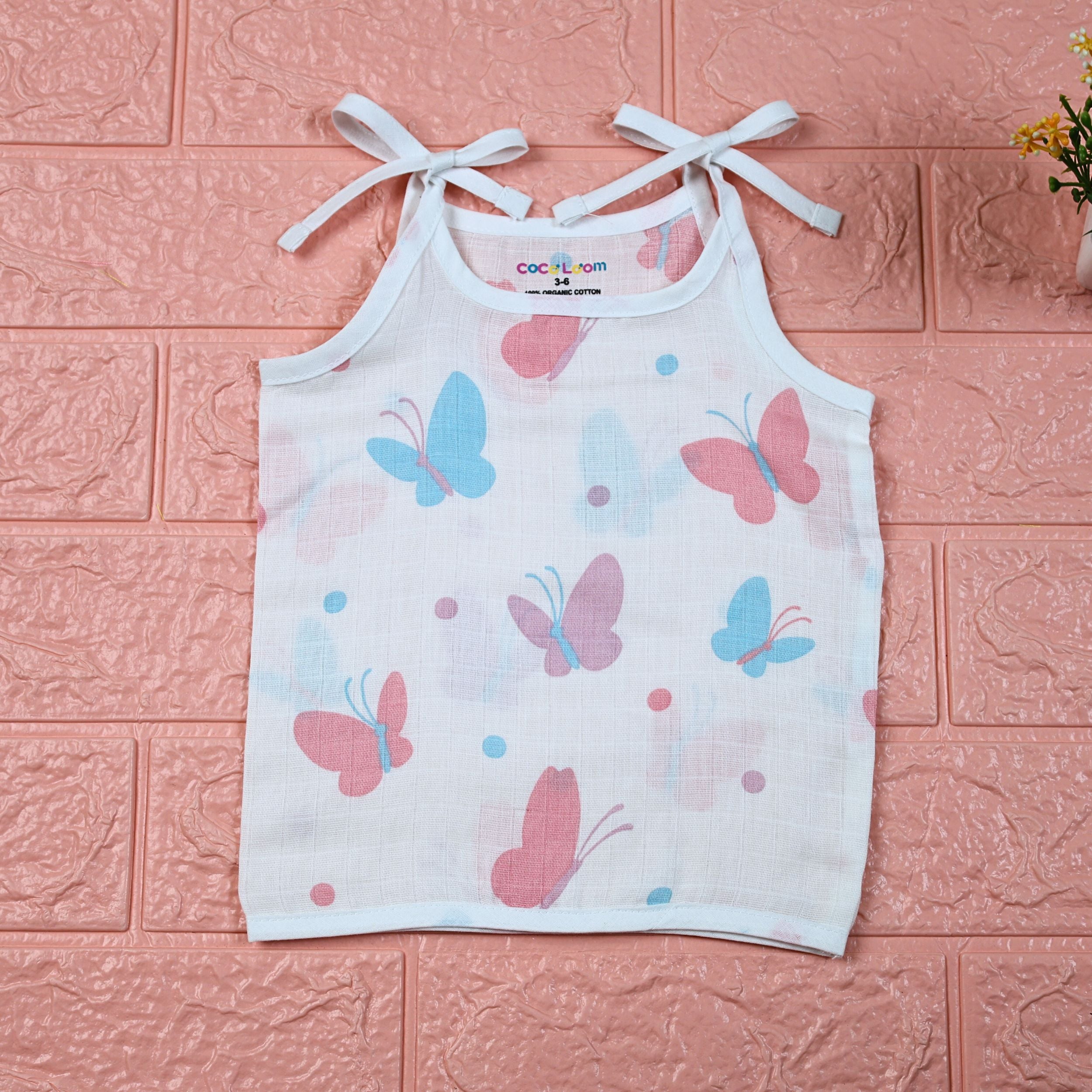Butterfly Blush baby top in white with tie-up shoulders, printed with pastel butterfly motifs in soft pink and blue tones.