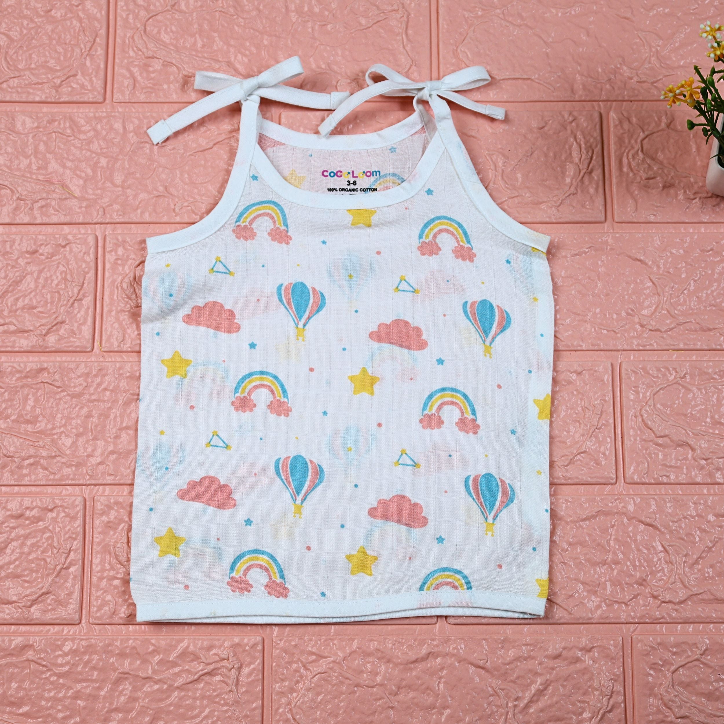 Rainbow Rides baby top in white with tie-up shoulders, printed with rainbows, air balloons, clouds, and stars.