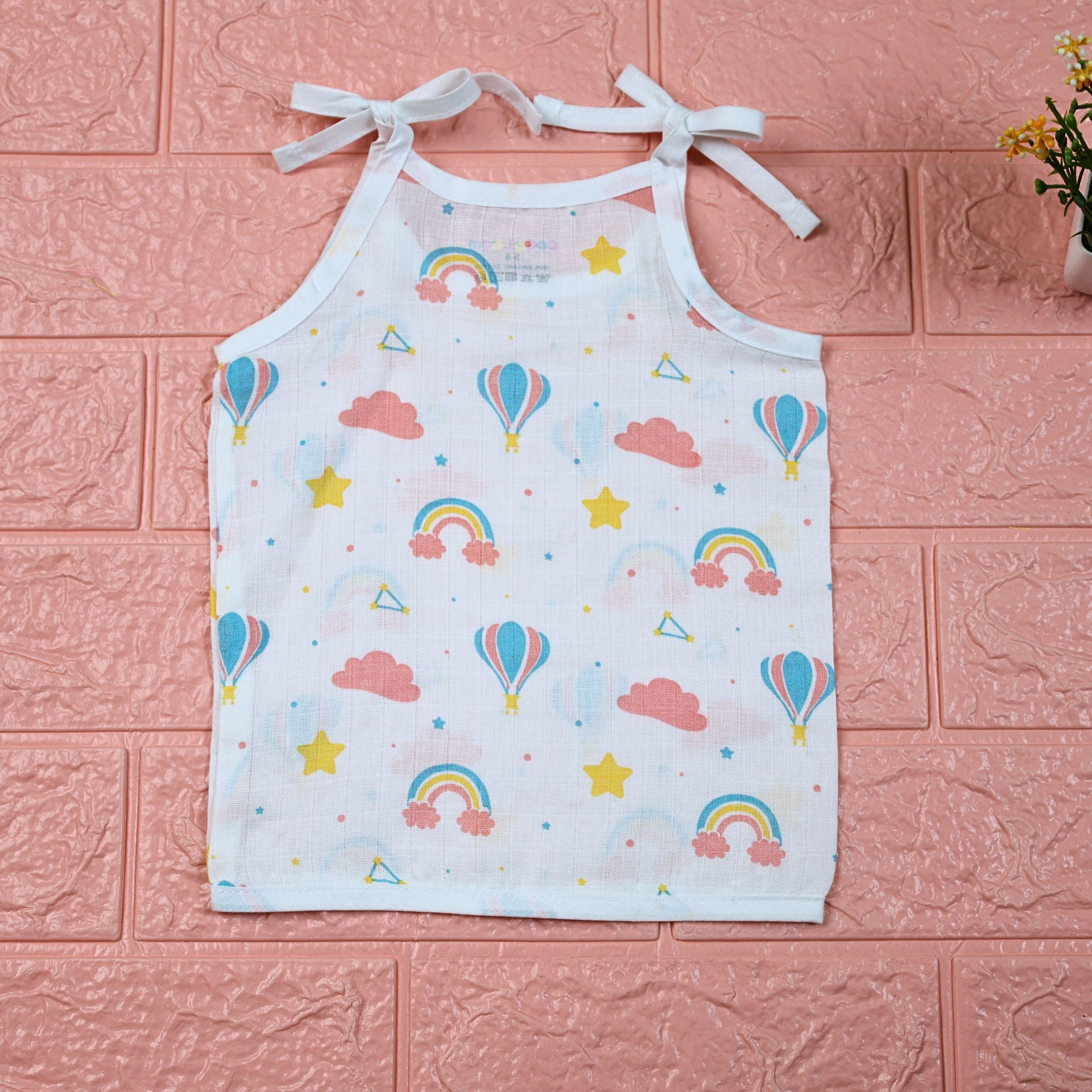 Rainbow Rides baby top in white with tie-up shoulders, printed with rainbows, air balloons, clouds, and stars.