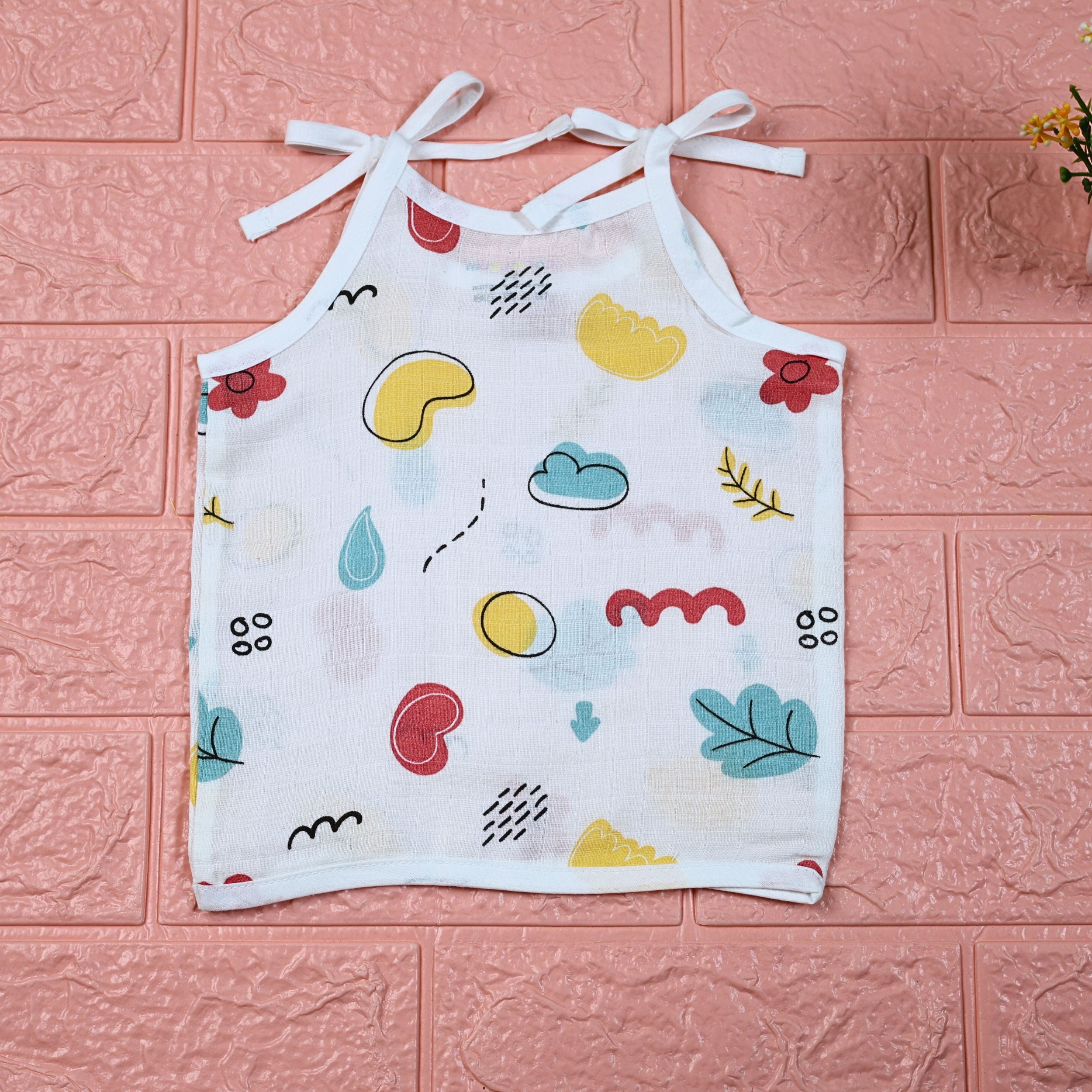 Wild Doodles baby top in white with shoulder knots, yellow, red and pastel green scribble patterns.