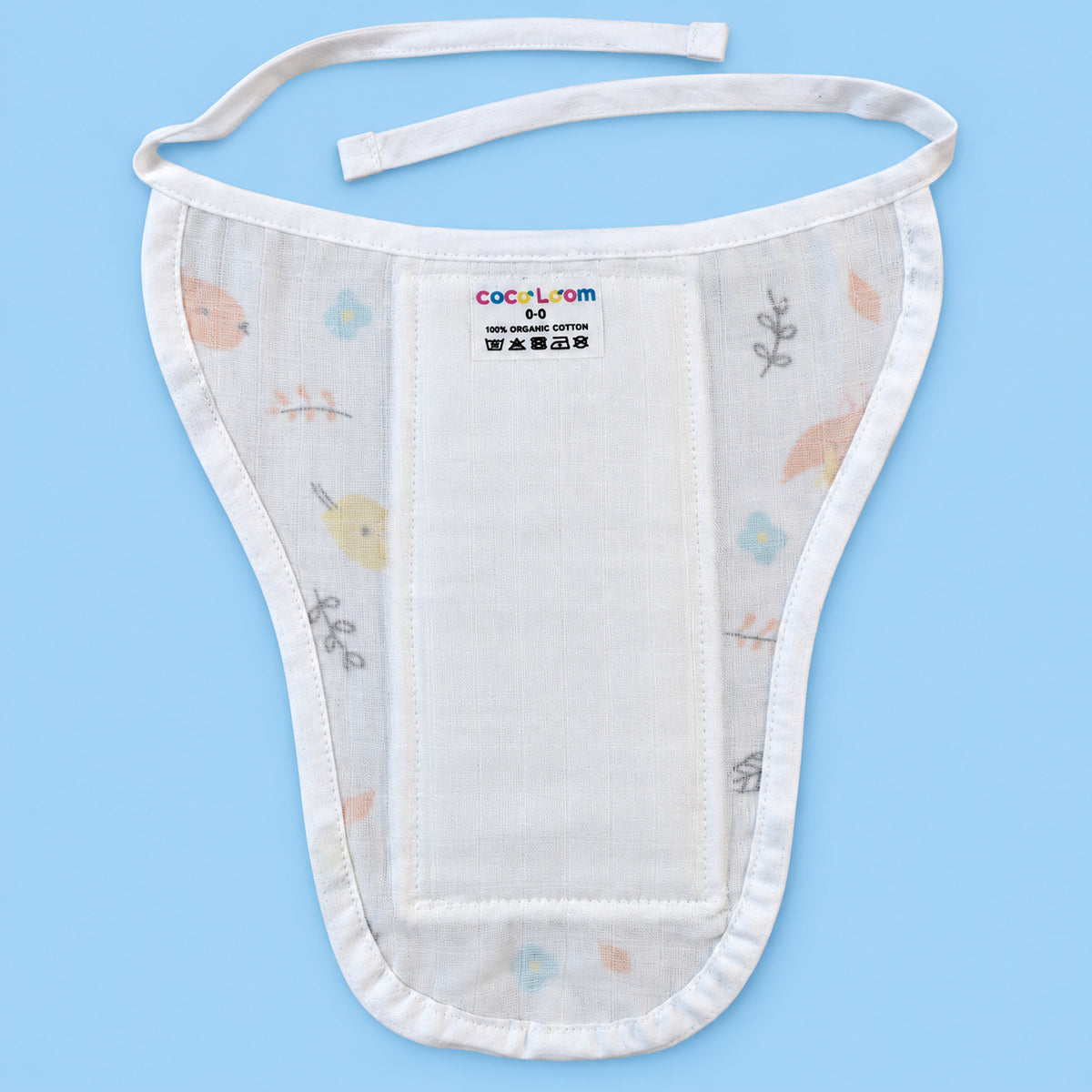 A white muslin baby bib with delicate pastel floral and bird patterns, featuring adjustable ties and a central patch set against a solid light blue background.